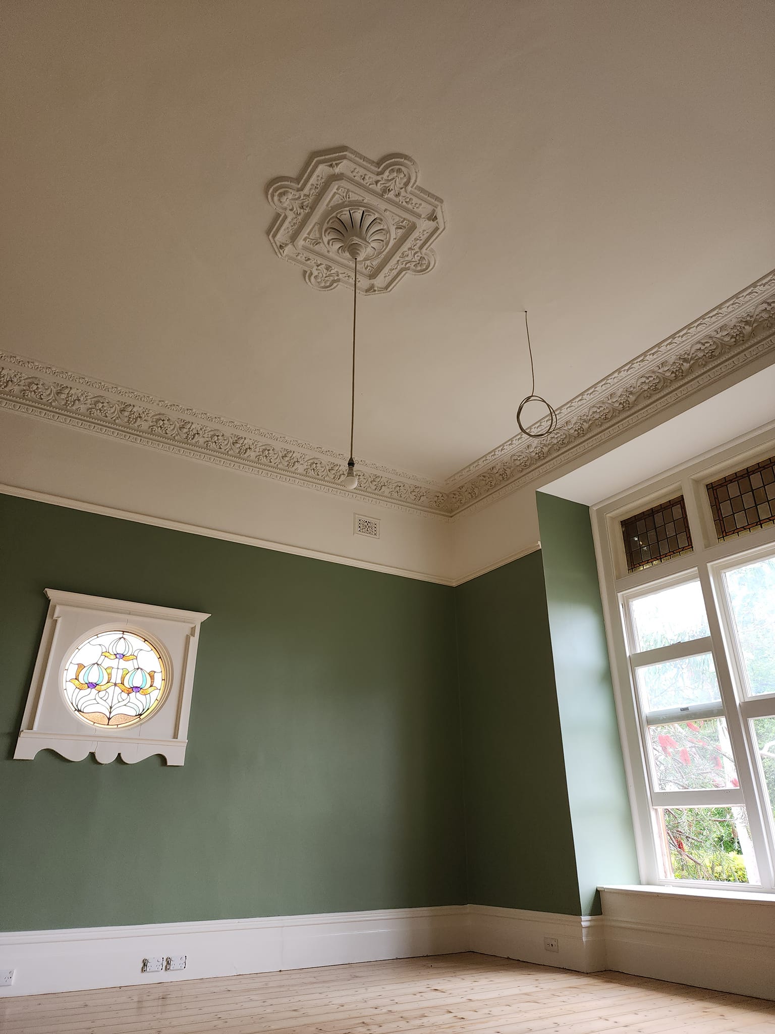 Heritage ceiling rose and acanthus cornice above sage green walls and a round stained glass window